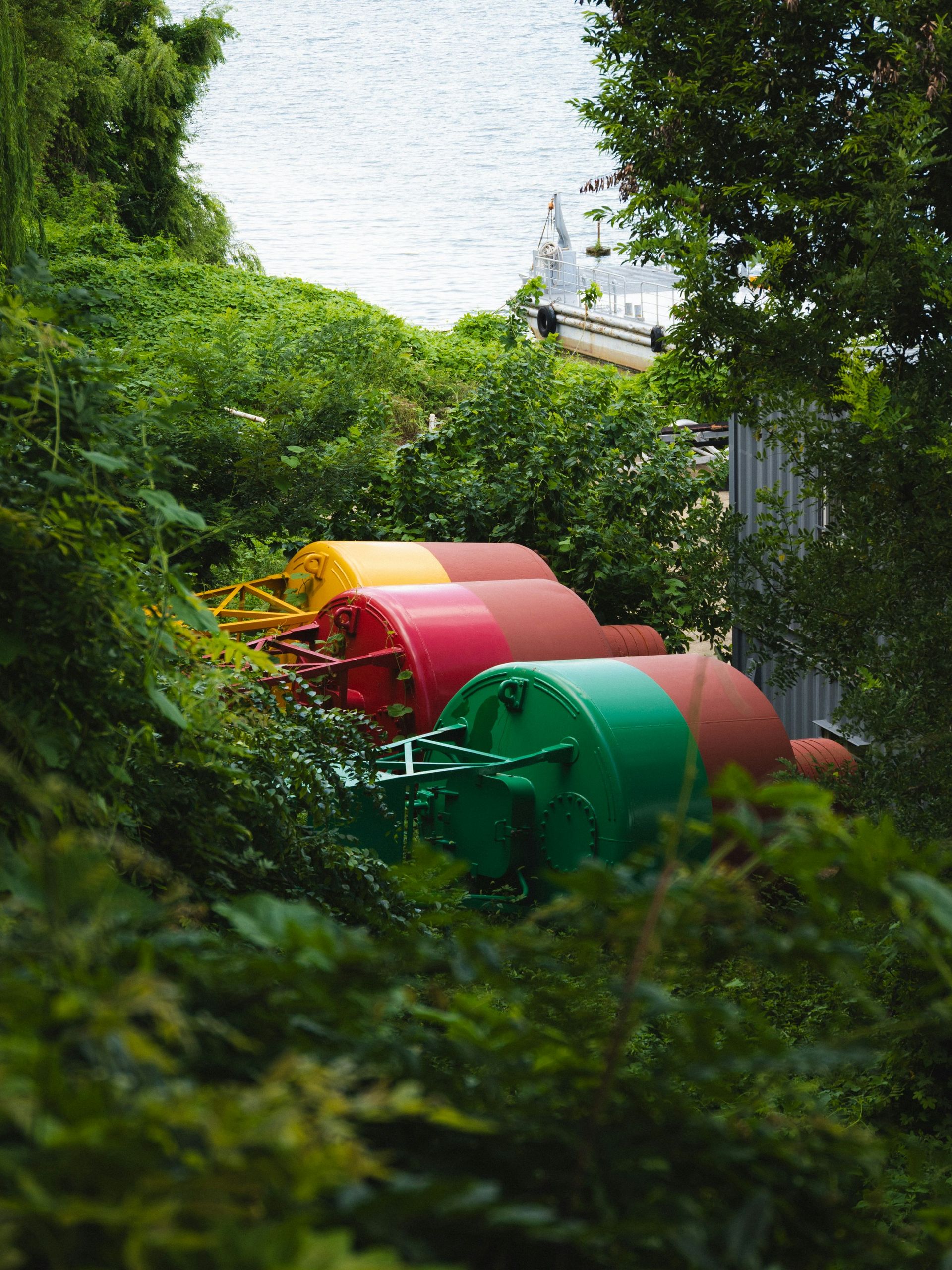 Three large cylindrical navigation buoys in yellow, red, and green nestled among lush foliage