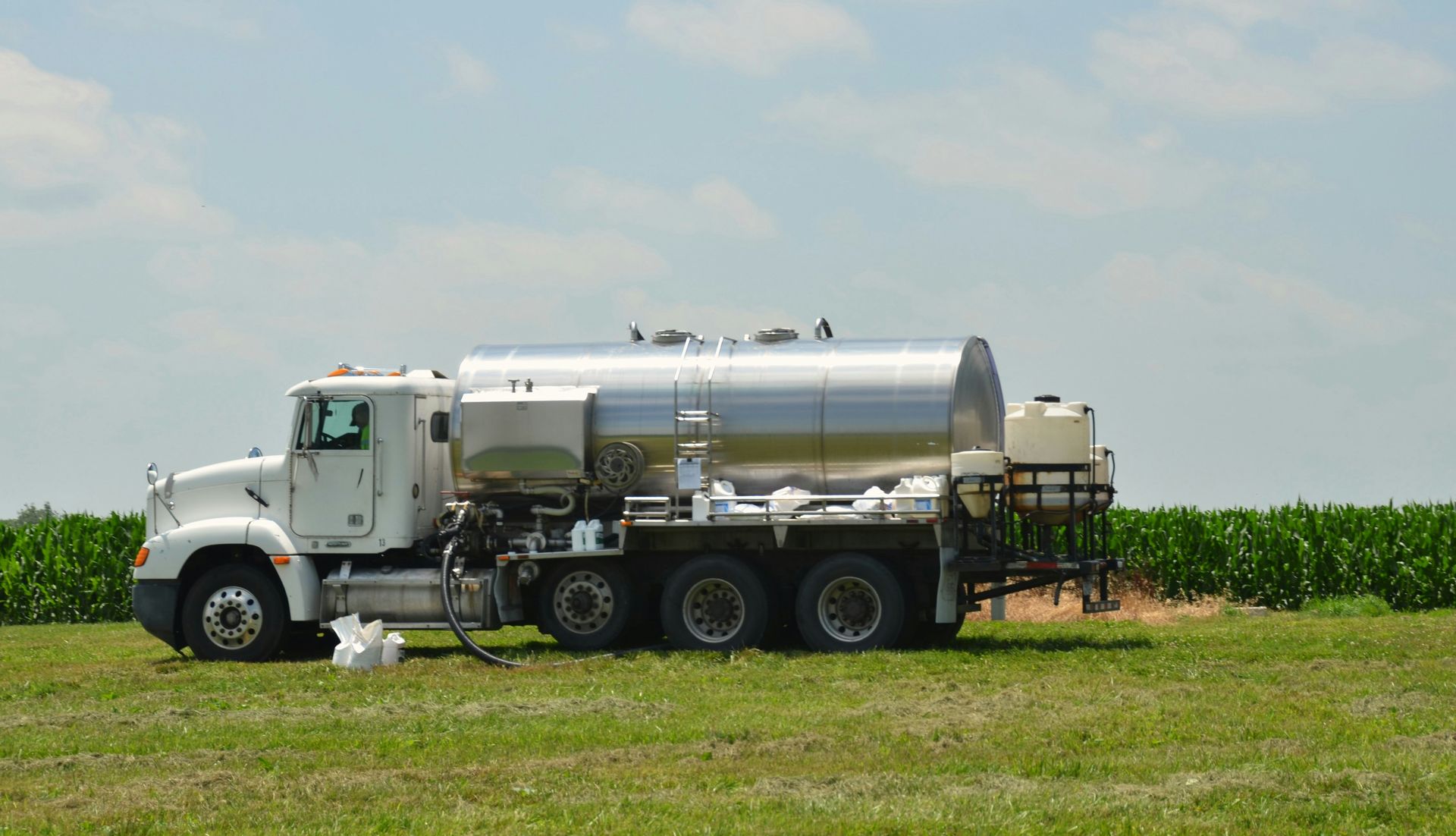 A white tanker truck spraying liquid in a green field