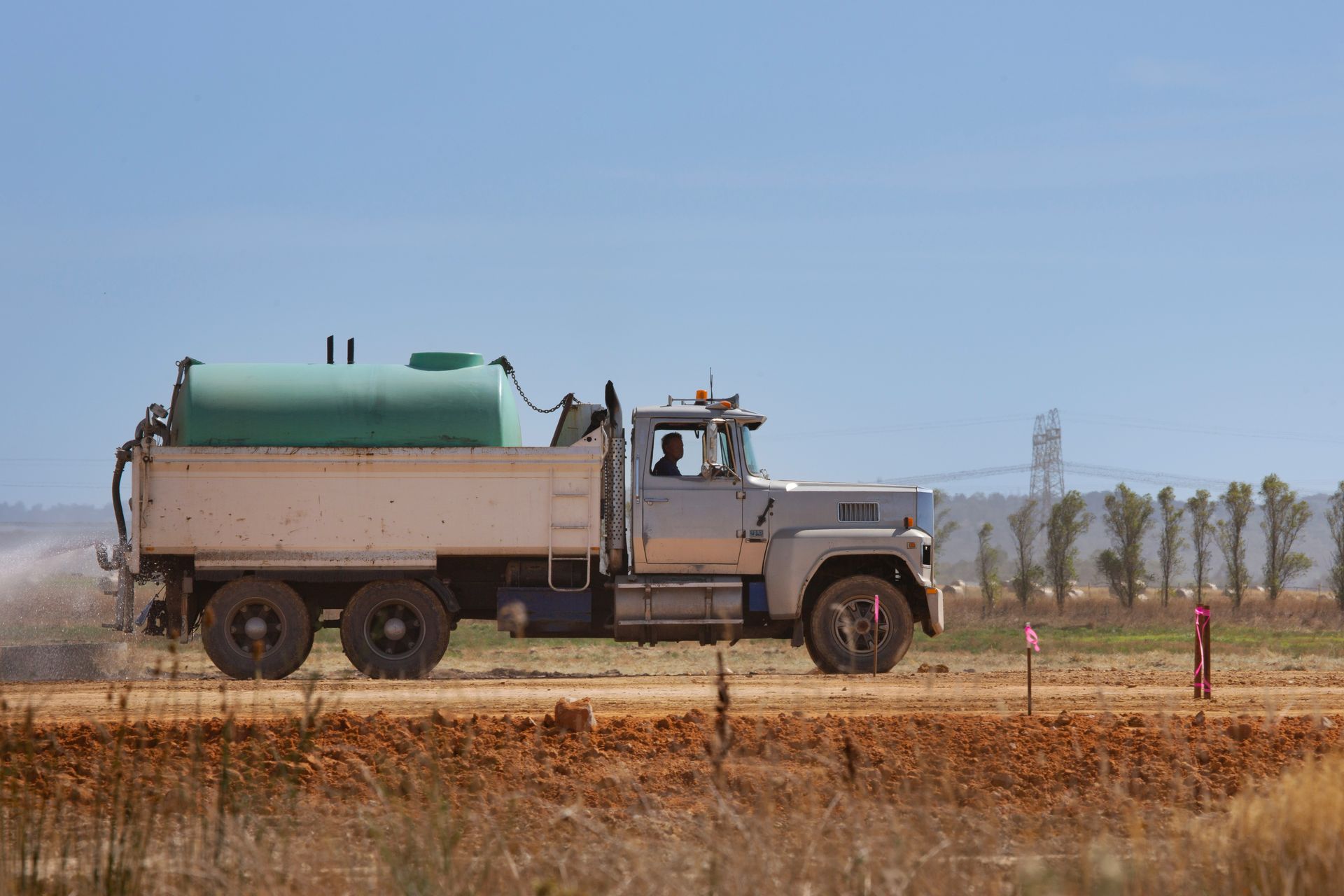 a truck driving down a dirt road next to a field